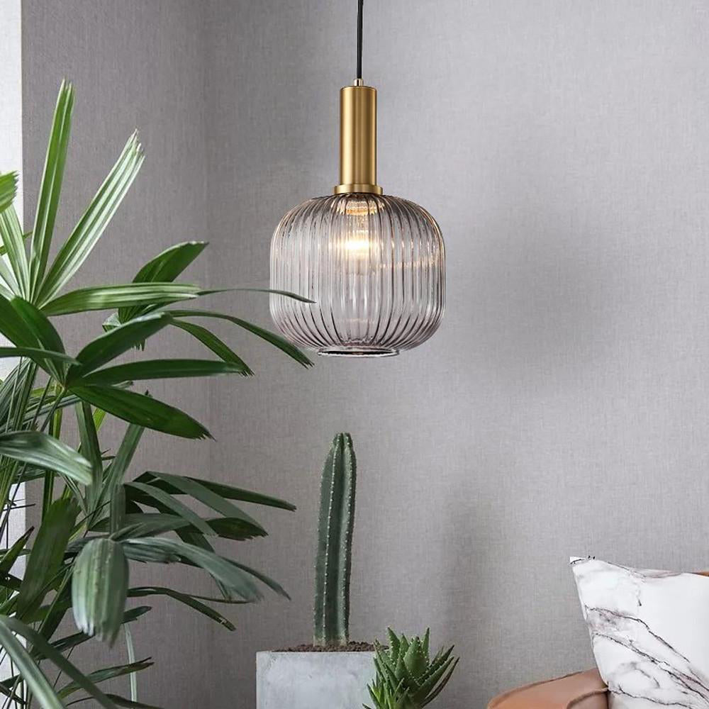 Smoke grey reeded glass pendant from Clérachic on a gold stem with its bulb visible, hanging against a grey wall beside a leafy plant and a cactus.