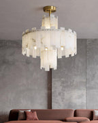 The Clérachic Regina chandelier lit in a concrete-walled room above a dusty pink sofa.