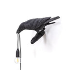 This black resin Clérachic bird lamp sits isolated on white, its clear bulb unlit and cord draping toward the floor.