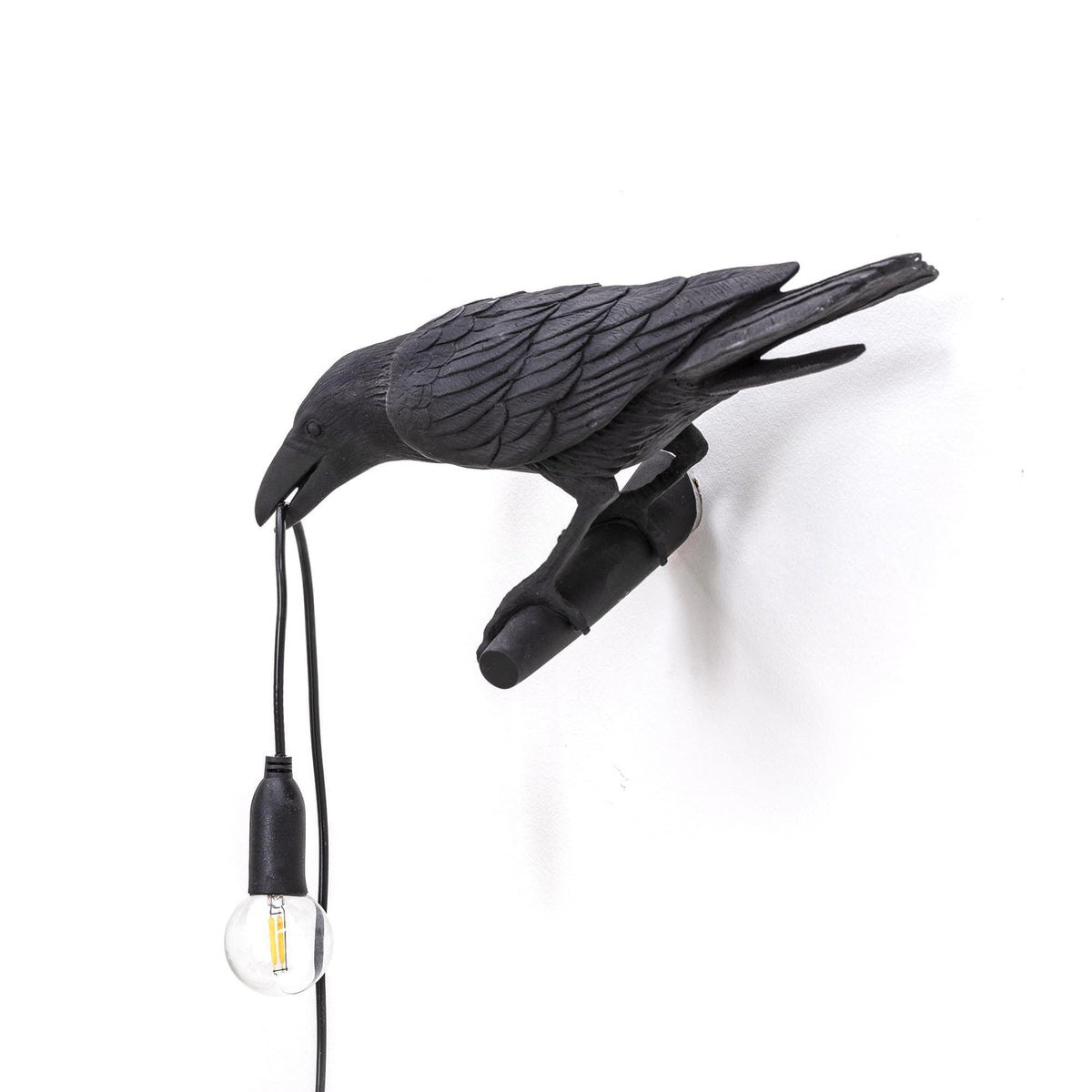 This black resin Clérachic bird lamp sits isolated on white, its clear bulb unlit and cord draping toward the floor.