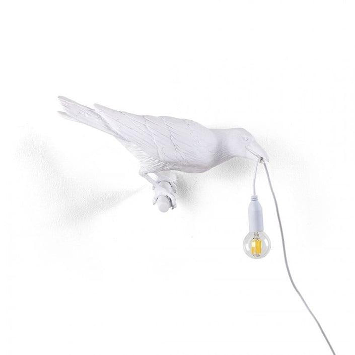 This white resin Clérachic bird lamp is shown in full profile, wings extended, its bulb glowing warm on white.