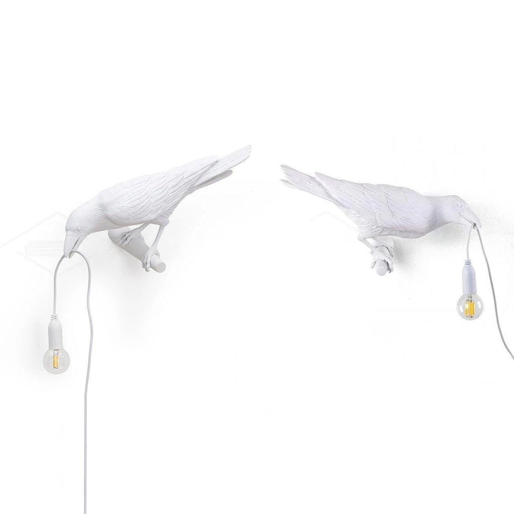 Two white Clérachic bird lamps stand side by side in mirrored poses, each holding a bulb by its beak.