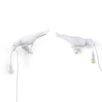 Two white Clérachic bird lamps stand side by side in mirrored poses, each holding a bulb by its beak.