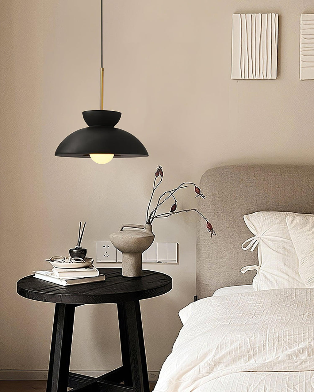 Small black dome pendant from Clérachic above a bedside table with a vase and books, beside a made-up bed.