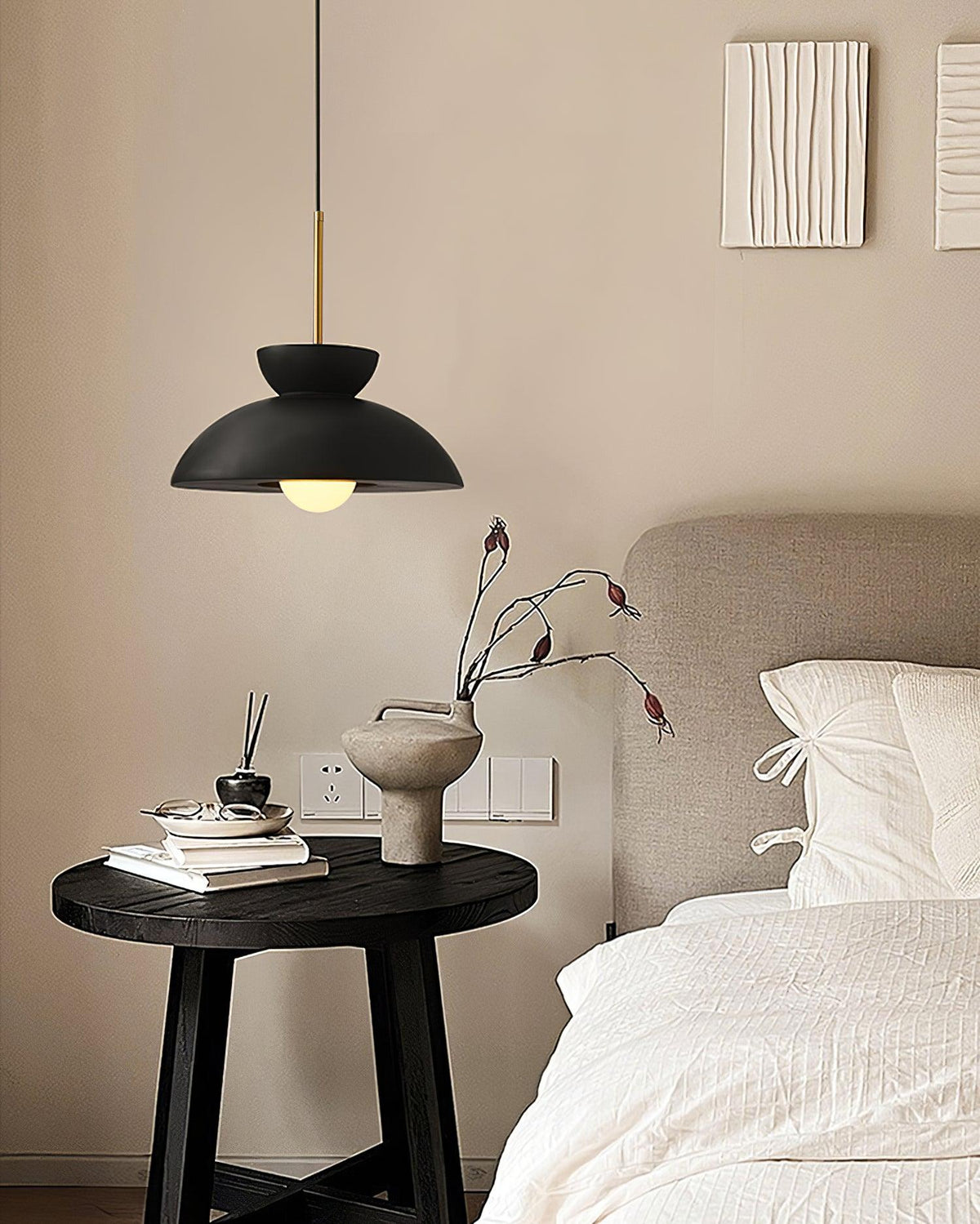 Small black dome pendant from Clérachic above a bedside table with a vase and books, beside a made-up bed.