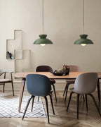Two green dome pendants from Clérachic hang over a wooden dining table with blue and taupe moulded chairs.