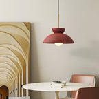 Red dome pendant from Clérachic hung in front of a tall arched artwork, with a round white table and tan chairs below.