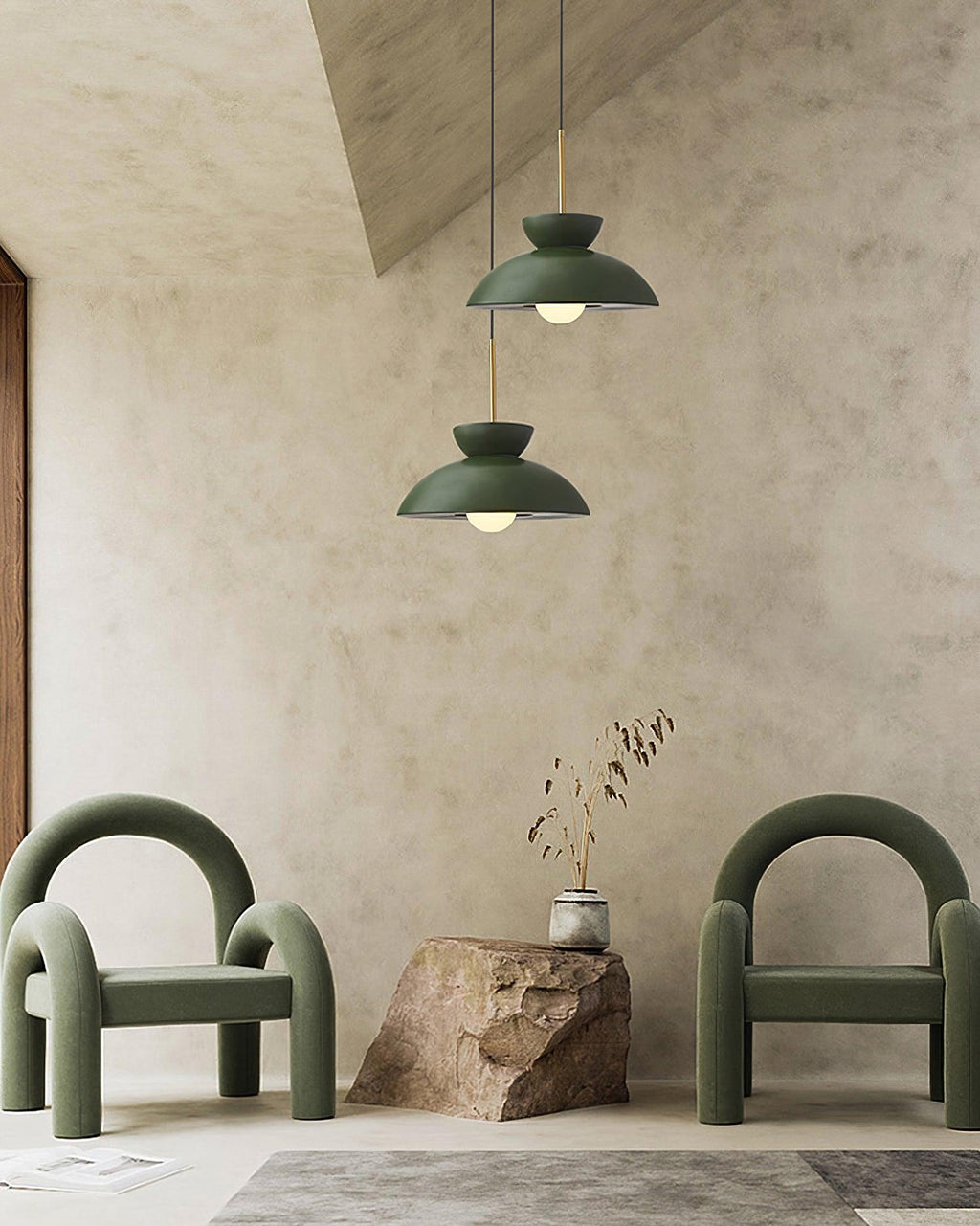 Two green dome pendants from Clérachic hang at different heights over green armchairs and a rough stone block.