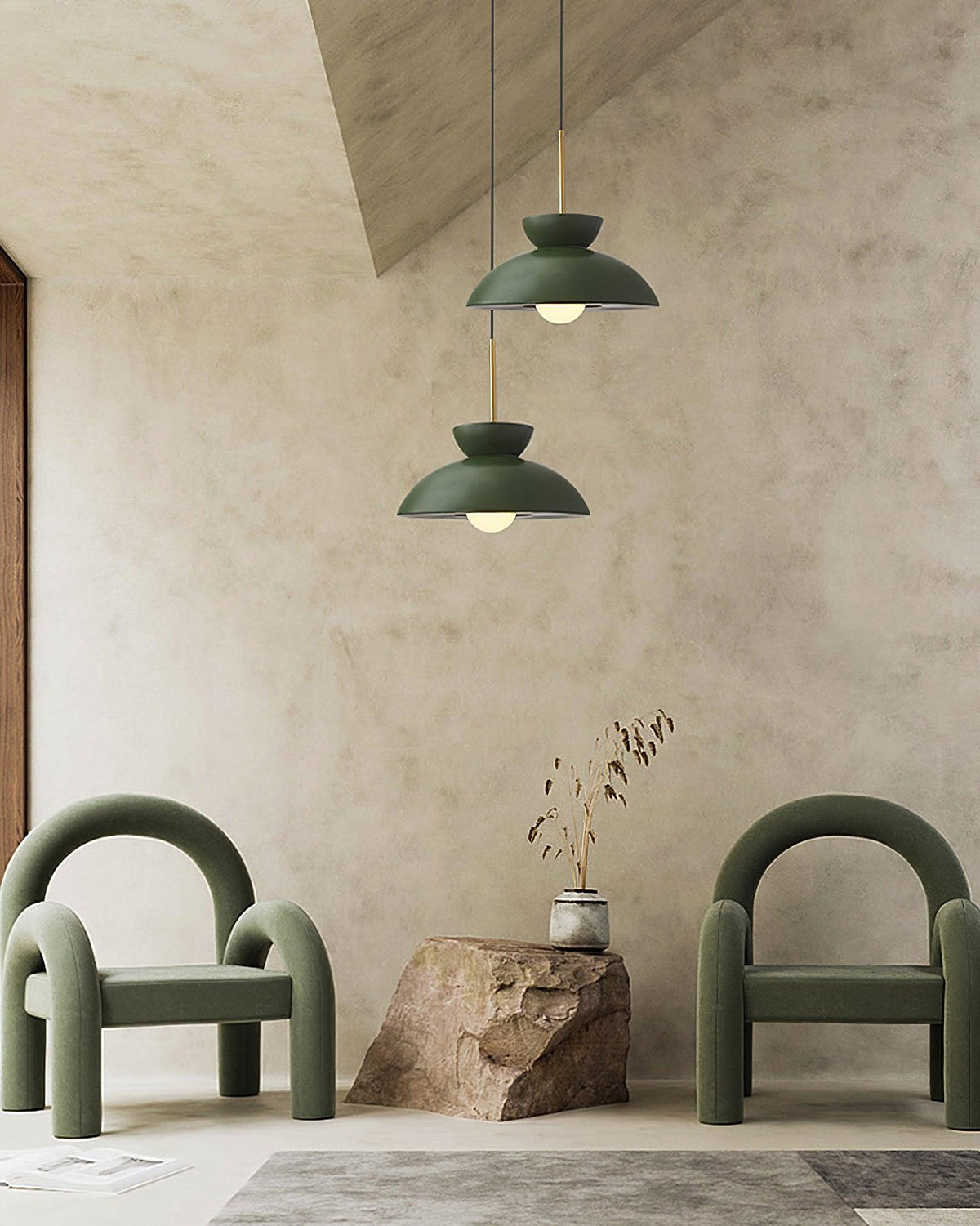 Two green dome pendants from Clérachic hang at different heights over green armchairs and a rough stone block.