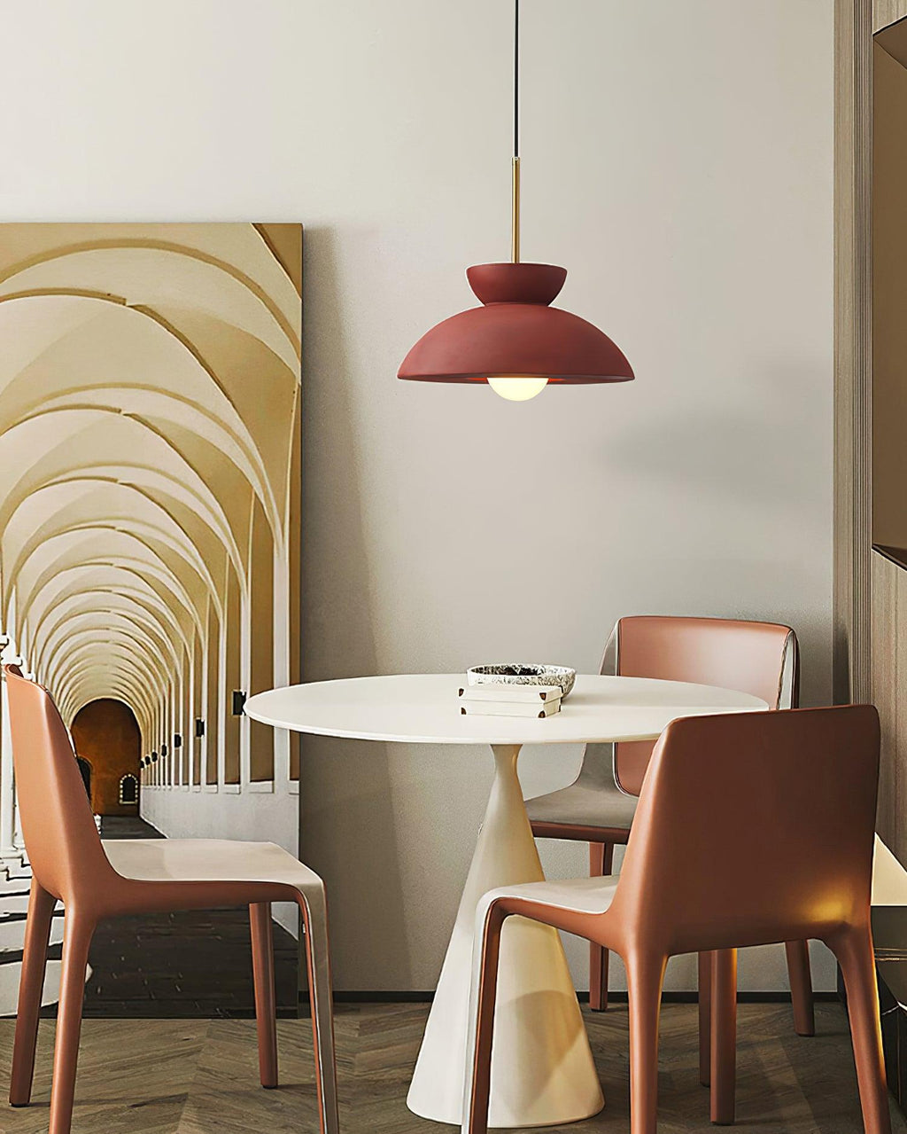 Red dome pendant from Clérachic above a white pedestal table and terracotta chairs, with an arched hallway artwork behind.
