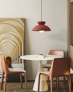 Red dome pendant from Clérachic above a white pedestal table and terracotta chairs, with an arched hallway artwork behind.