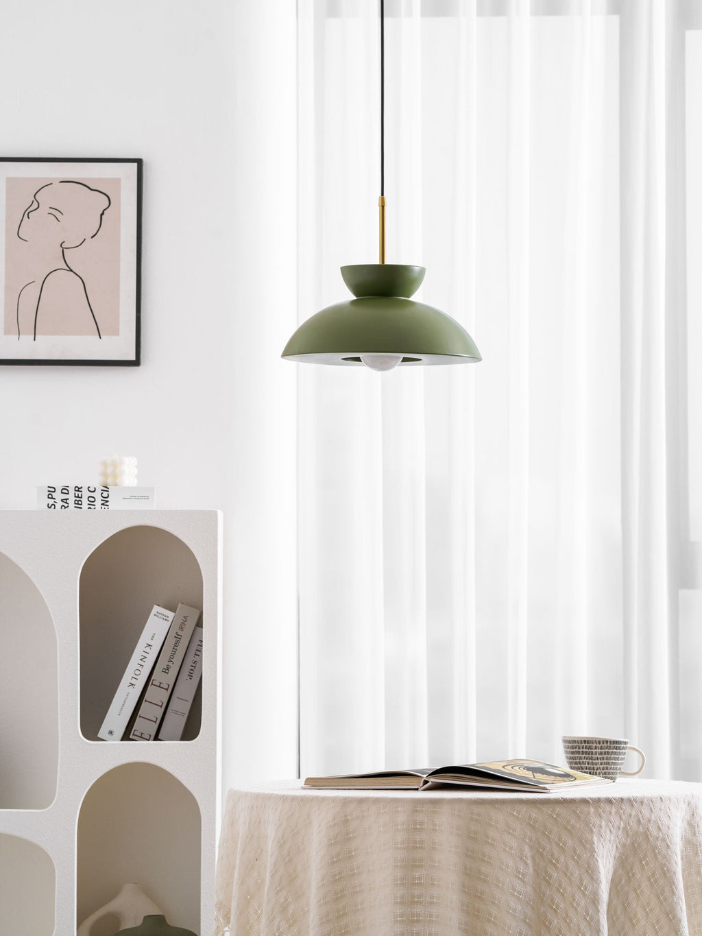 Green dome pendant from Clérachic lit from within, in a white room with a draped table and an open book below.