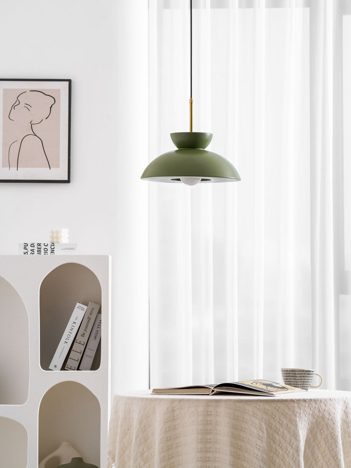 Green dome pendant from Clérachic lit from within, in a white room with a draped table and an open book below.