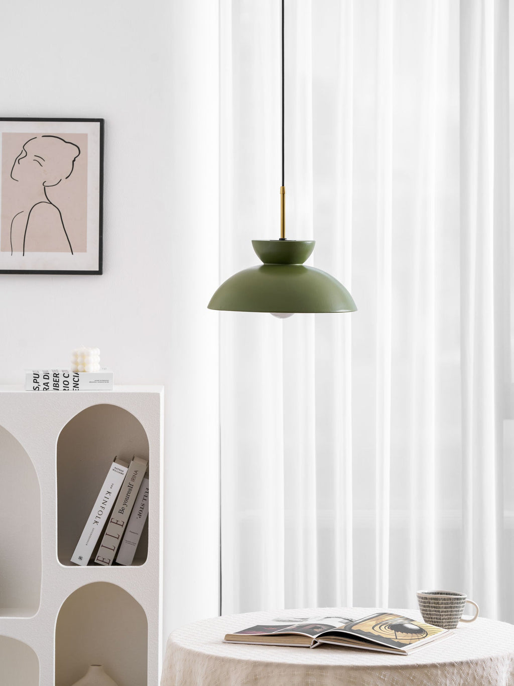 Green dome pendant from Clérachic hung beside curtains, with a patterned print and a book on the table below.