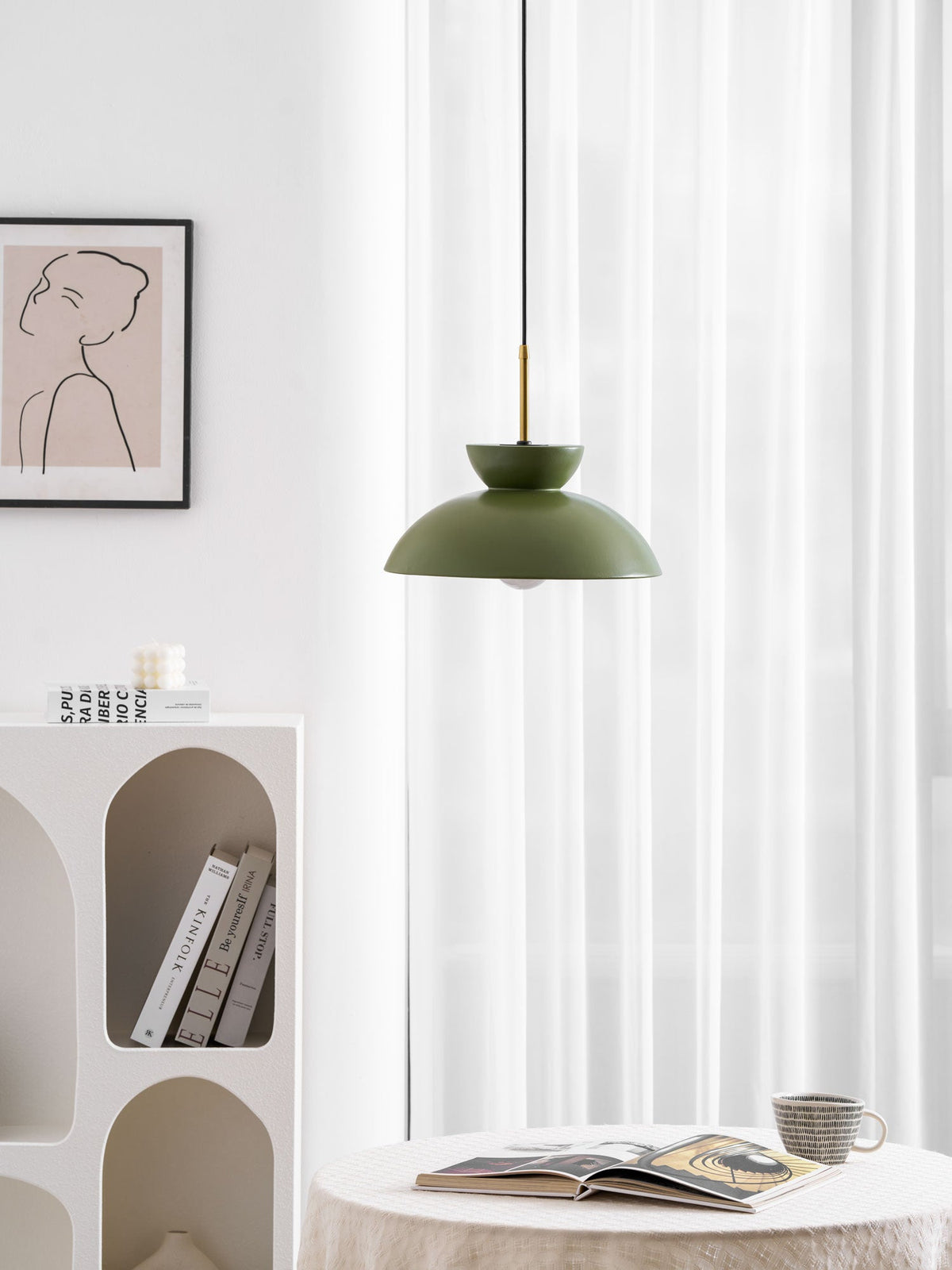Green dome pendant from Clérachic hung beside curtains, with a patterned print and a book on the table below.