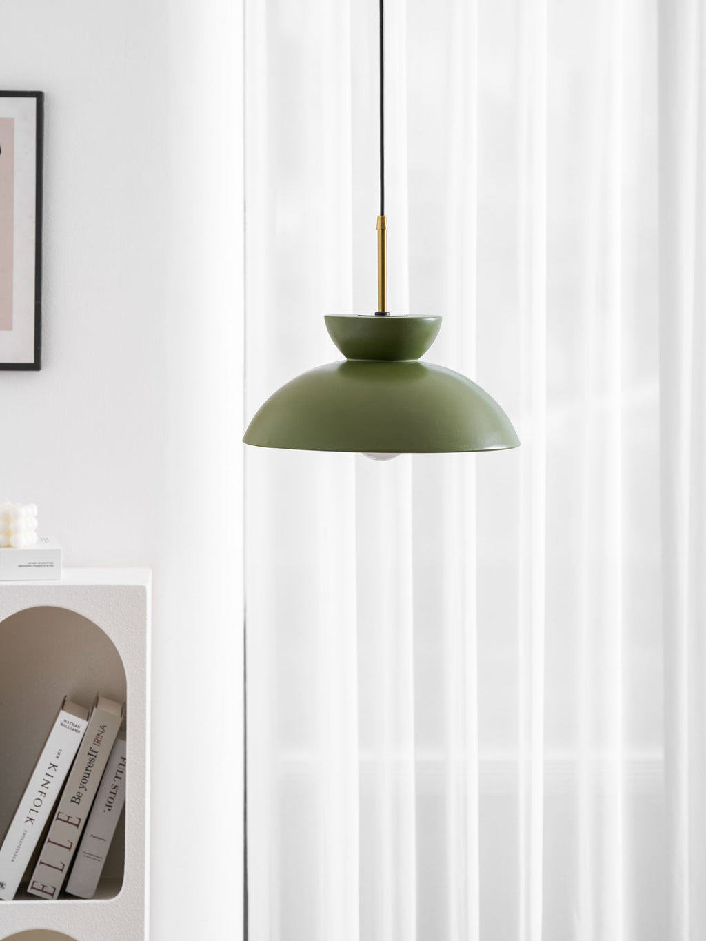 Cropped view of the green Clérachic pendant against white curtains, with the brass stem and an arched shelf at the edge.