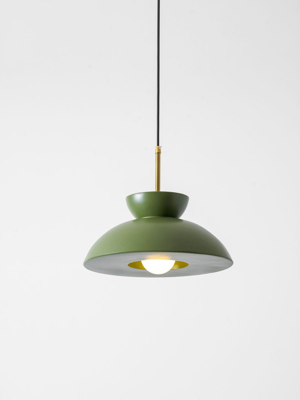 Green dome pendant from Clérachic with a lit bulb and a brass-toned ring inside the shade, on a pale backdrop.