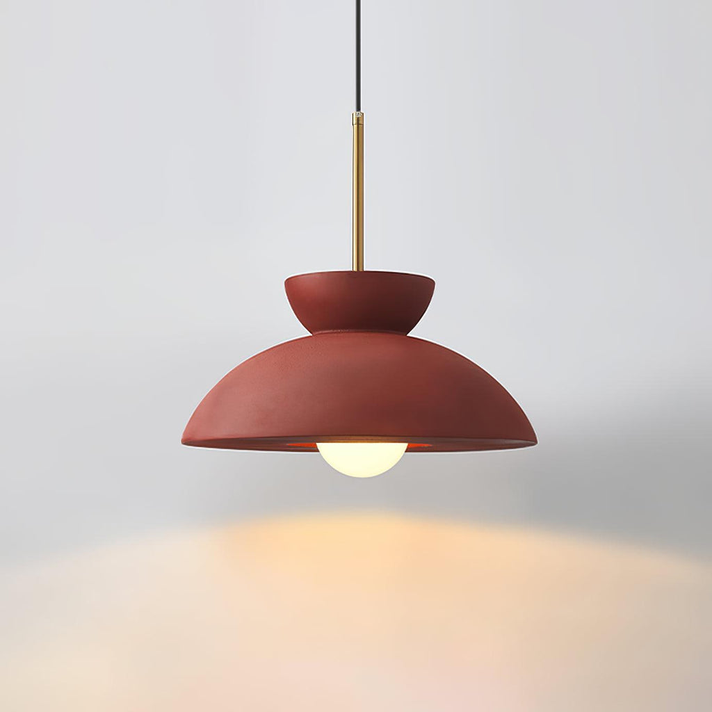 Red dome pendant from Clérachic on a grey backdrop, its bulb casting a warm glow below.