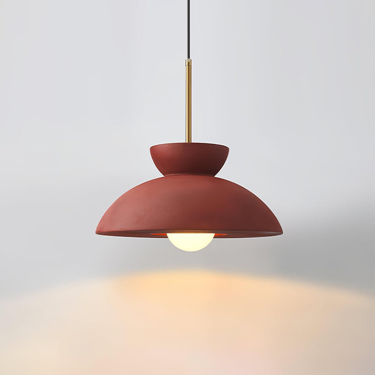Red dome pendant from Clérachic on a grey backdrop, its bulb casting a warm glow below.