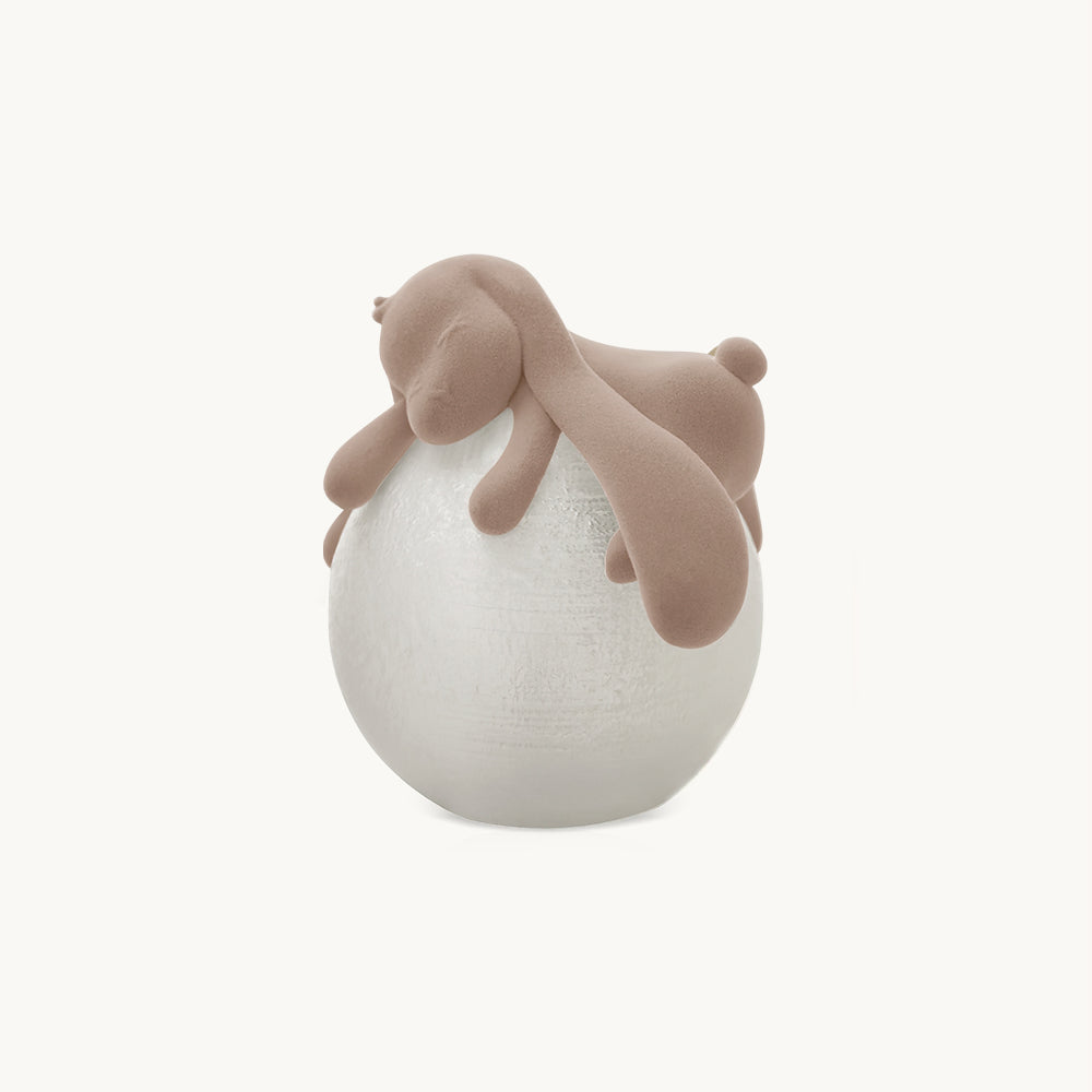 A flocked rabbit curled over a white textured globe, shown as a Clérachic table lamp on a plain off-white backdrop.