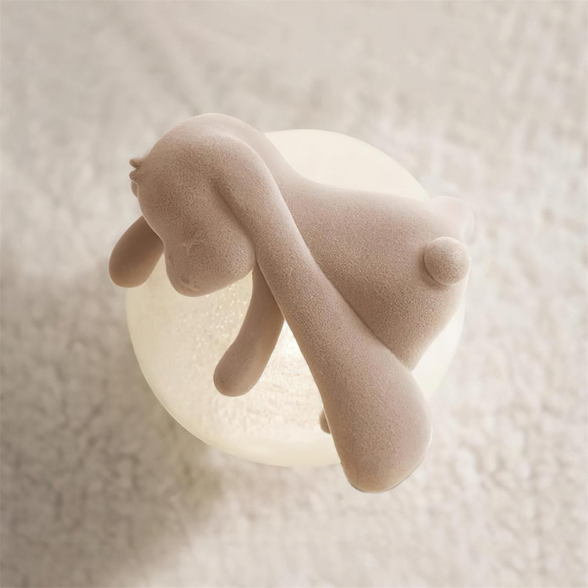 Close view of the long flocked ears and warm glowing globe of this Clérachic rabbit lamp, on a cream boucle throw.