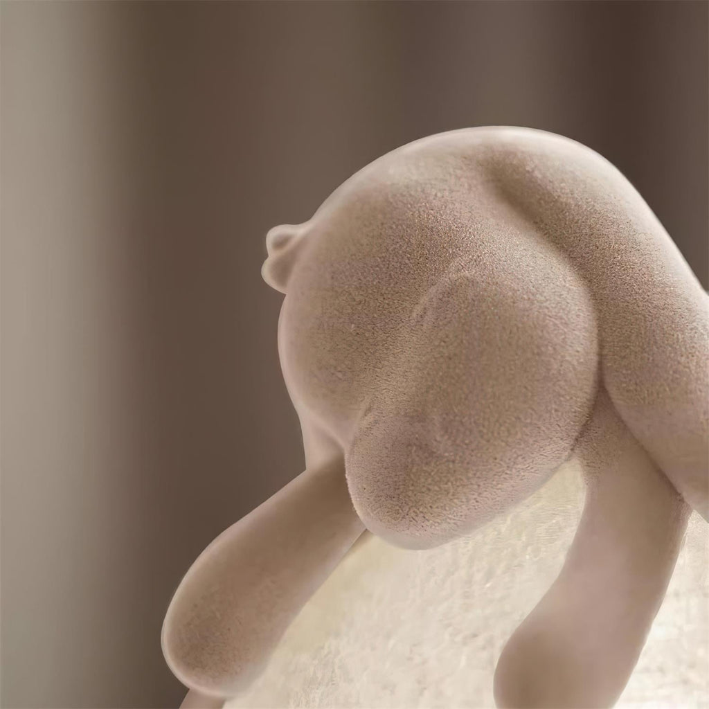 Close view of the soft flocked head and ear of the rabbit on this Clérachic lamp, with the globe glowing behind.