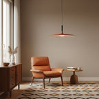 This Clérachic orange disc pendant hangs in a warm beige room above a tan leather armchair and a patterned rug.