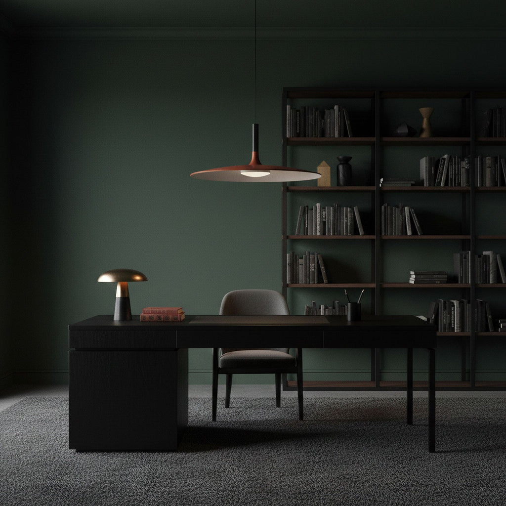 Clérachic disc pendant light in a dark green study, hanging above a black desk with a small lamp and a bookcase behind.