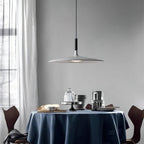 A grey Clérachic pendant light over a round table dressed with a navy cloth, with white curtains and dark chairs behind.
