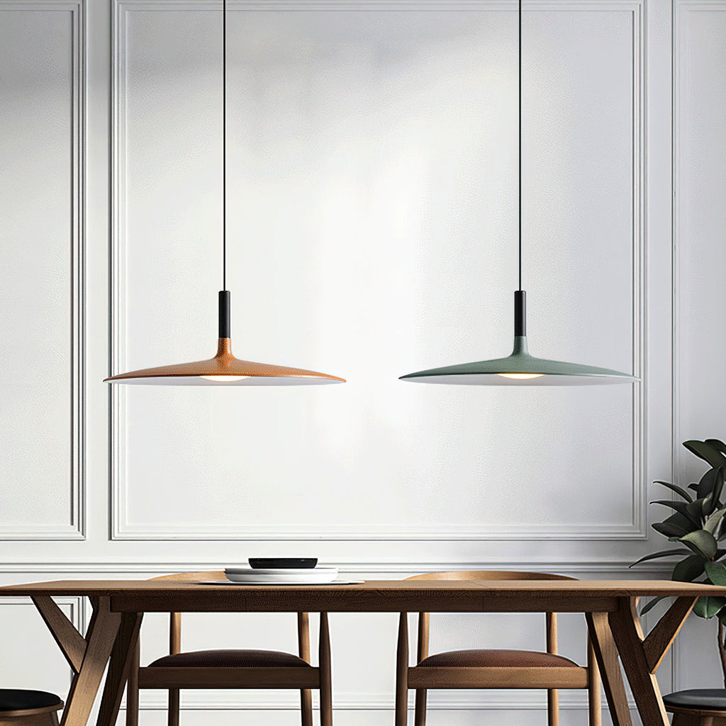 Clérachic pendants in orange and green hanging side by side above a wooden dining table, in front of a white panelled wall.