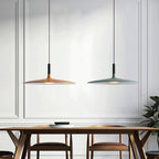 Clérachic pendants in orange and green hanging side by side above a wooden dining table, in front of a white panelled wall.
