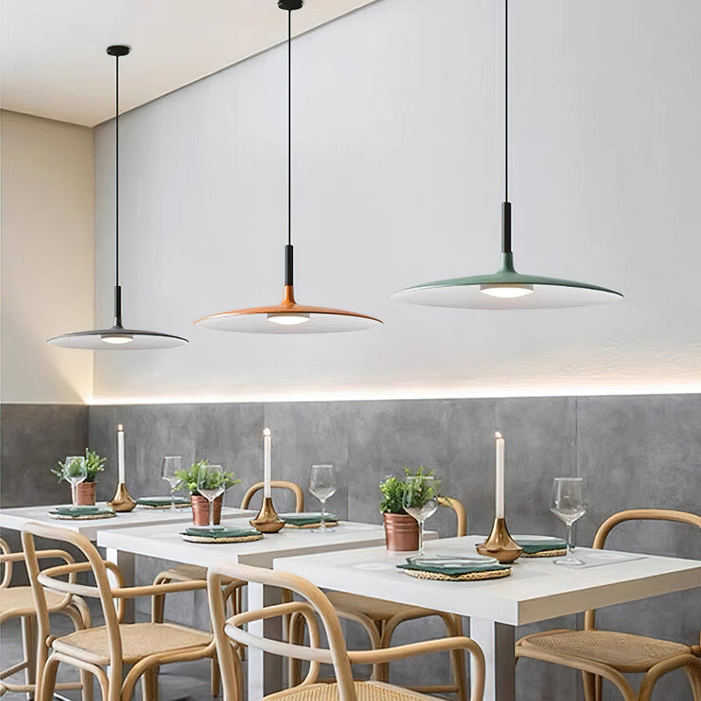 A row of three Clérachic pendants in grey, orange and green above white restaurant tables, with warm light along the wall.