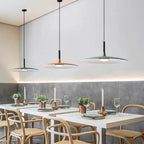 A row of three Clérachic pendants in grey, orange and green above white restaurant tables, with warm light along the wall.