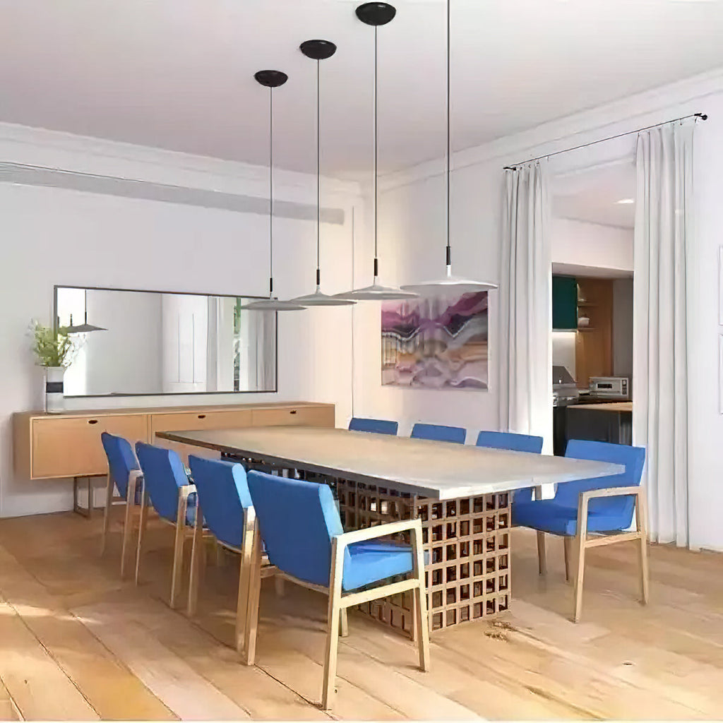 Four Clérachic pendants in white and grey hung in a line over a long dining table with blue chairs and a wood floor.