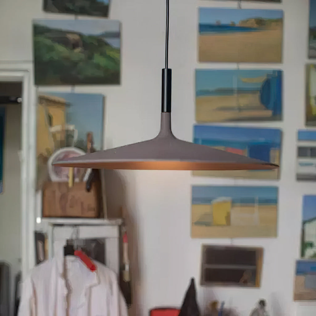 A Clérachic pendant in a dark brown finish in a studio with paintings of beach scenes pinned on the wall.