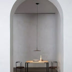 Single Clérachic pendant light hung in a plastered arch, above a small wooden table with two black chairs.