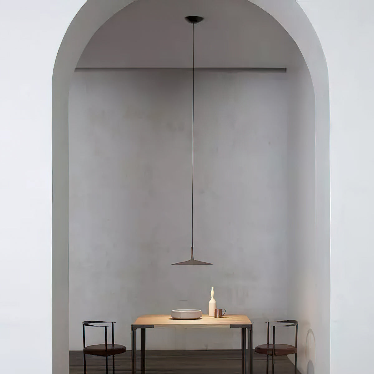 Single Clérachic pendant light hung in a plastered arch, above a small wooden table with two black chairs.