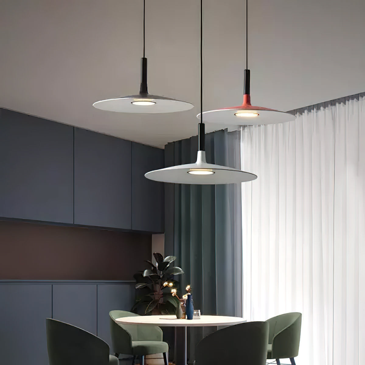 Three Clérachic pendants in grey and orange hung together in a dark dining room with blue-grey cabinets and green chairs.