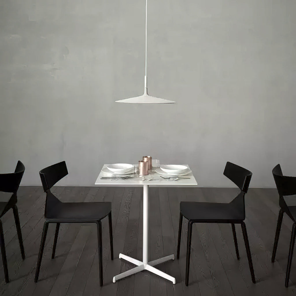 A pale Clérachic disc pendant above a white restaurant table with black chairs, in front of a grey concrete wall.