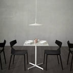A pale Clérachic disc pendant above a white restaurant table with black chairs, in front of a grey concrete wall.