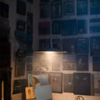 Clérachic pendant light with a dark shade, throwing warm light on a wall of framed pictures in a dim room.