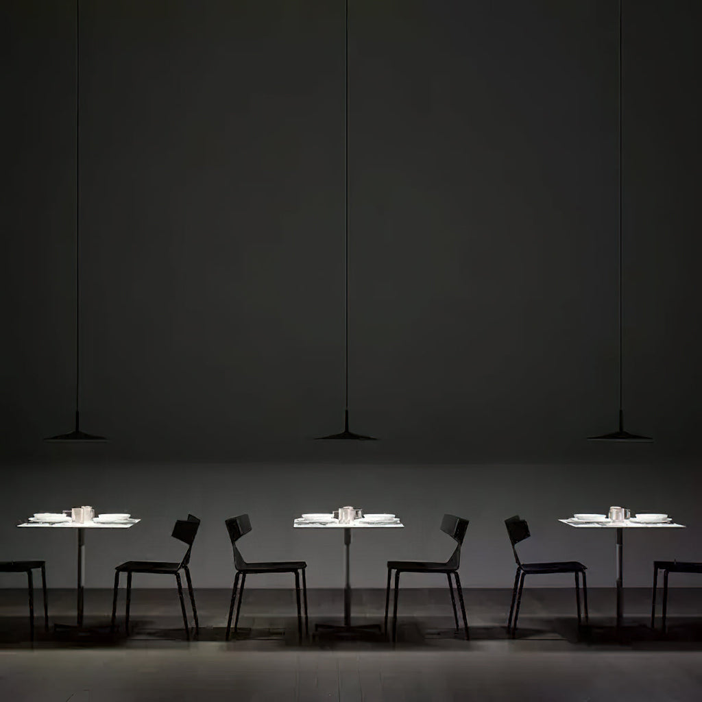 Three Clérachic pendants hung in a row over small white tables in a dark restaurant, each with black chairs around it.