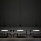 Three Clérachic pendants hung in a row over small white tables in a dark restaurant, each with black chairs around it.