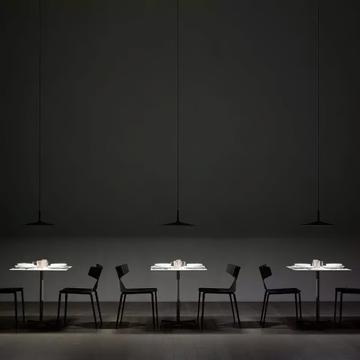 Three Clérachic pendants hung in a row over small white tables in a dark restaurant, each with black chairs around it.