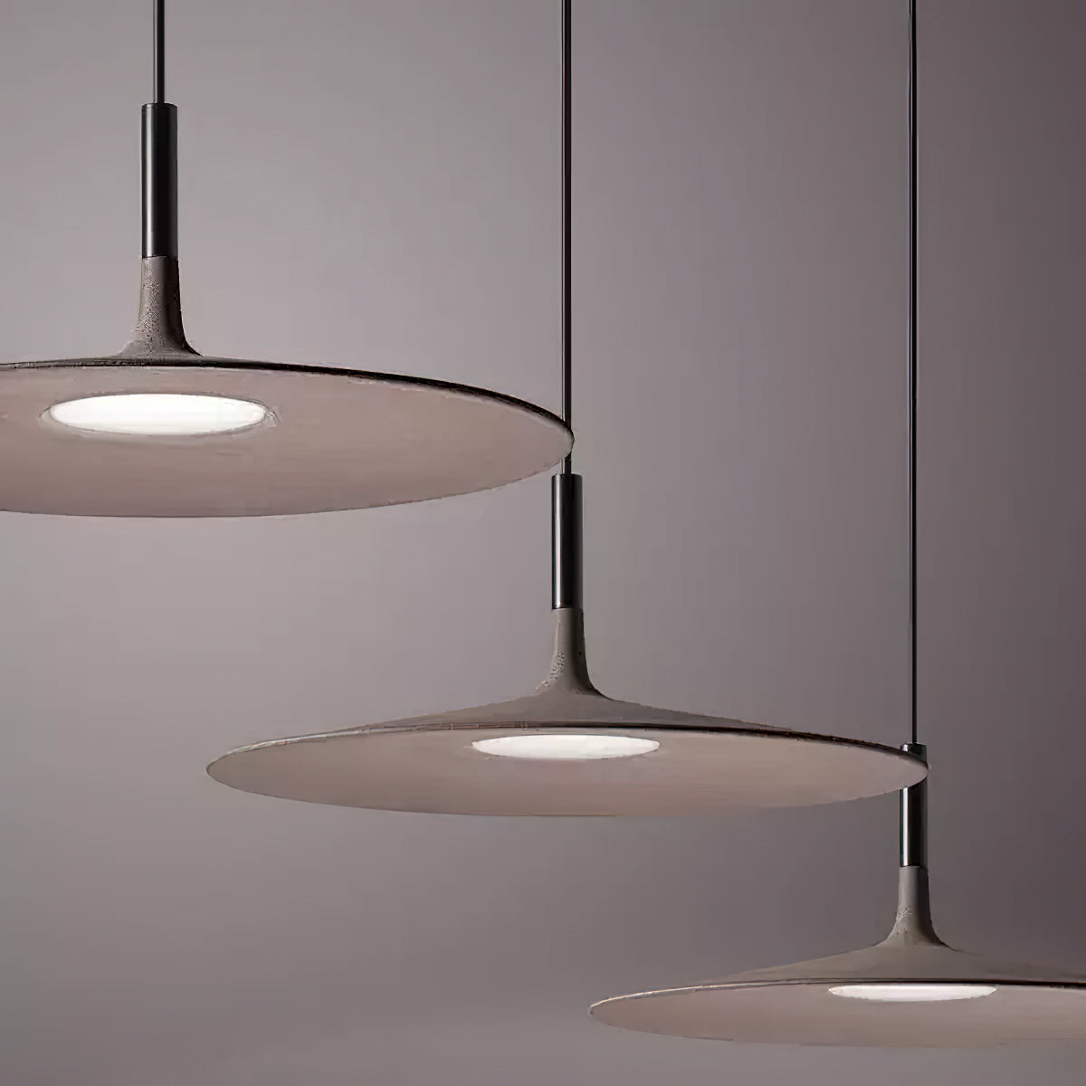 Close view of three overlapping Clérachic disc pendants in taupe, with the round lit diffuser underneath each one.