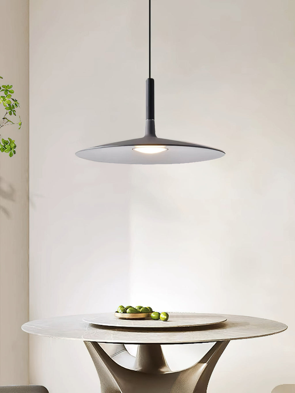 This Clérachic grey disc pendant is shown above a round stone table with a bowl of limes, in a bright room.