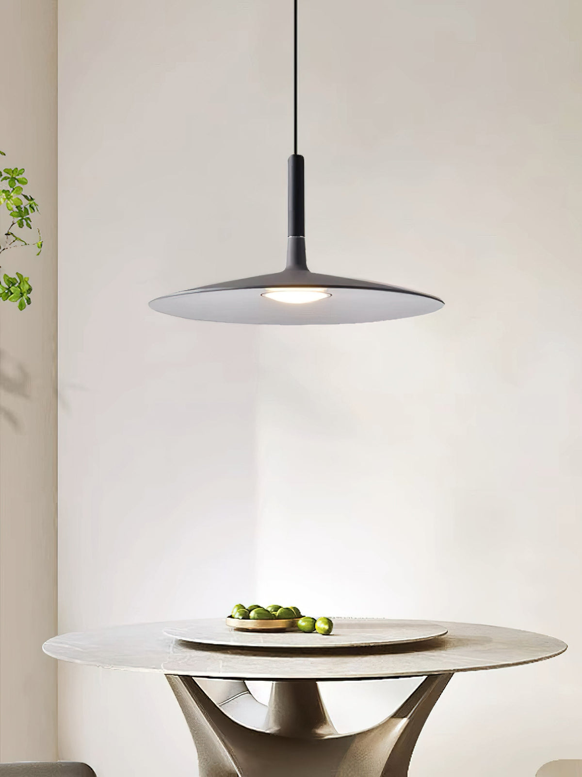 This Clérachic grey disc pendant is shown above a round stone table with a bowl of limes, in a bright room.