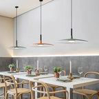 Three Clérachic pendants in grey, orange and green above restaurant tables, with warm light along a grey stone wall.