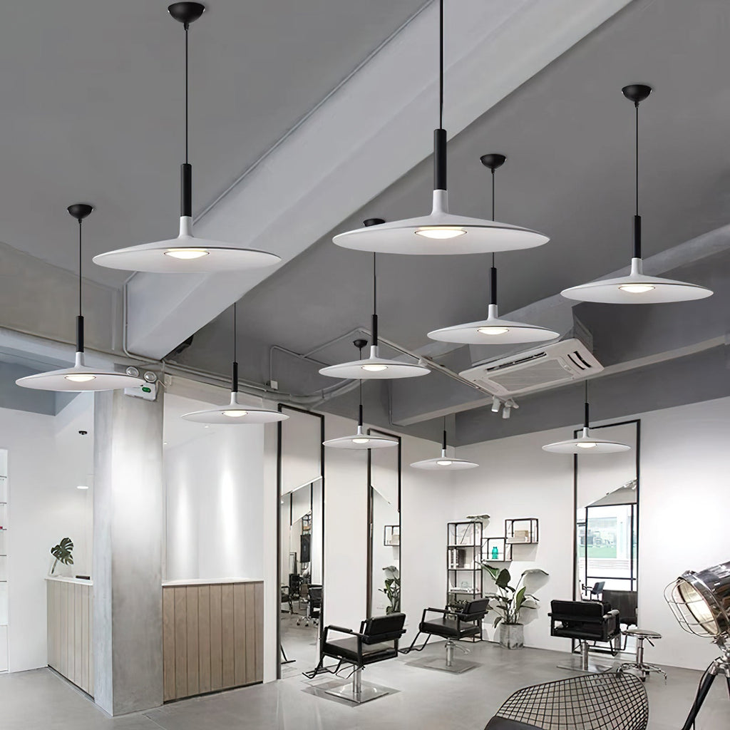 Many Clérachic disc pendants in white and grey hung at different heights in a bright salon with black chairs.