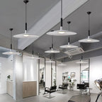 Many Clérachic disc pendants in white and grey hung at different heights in a bright salon with black chairs.